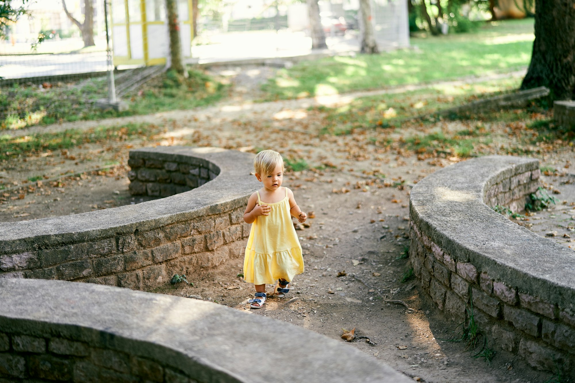 Little girl walks in the park near semicircular retaining stone walls